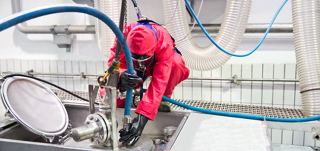 An operator in an red chemical splash resistant suit cleaning out a storage unit